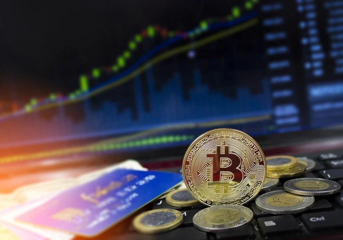 Cryptocurrency coins stacked on a keyboard in front of a screen showing stocks.