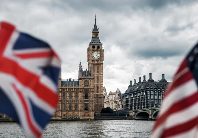Header graphic showing the Palace of Westminster and Big Ben in London under cloudy skies, with a blurred UK flag on the left and a blurred US flag on the right. A dark translucent banner across the lower half displays the EM360Tech logo and the headline: "UK and US Authorities Increase Pressure on AI Developers After Rogue Agent Incidents".