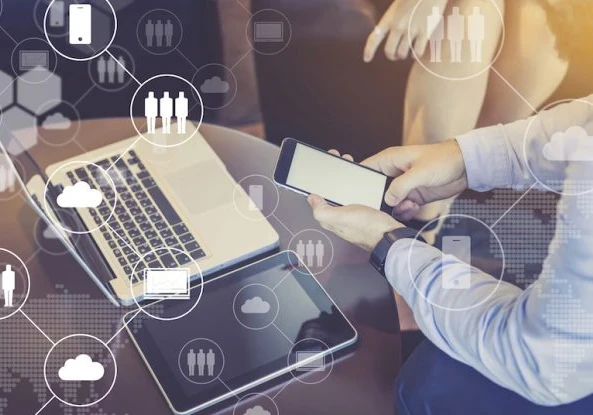 someone using a smartphone, with a macbook laptop and tablet next to them on a desk