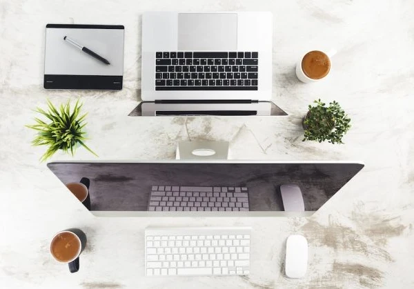 macbook and iMac computer on a desk with apple mouse and keyboard, and apple magic trackpad