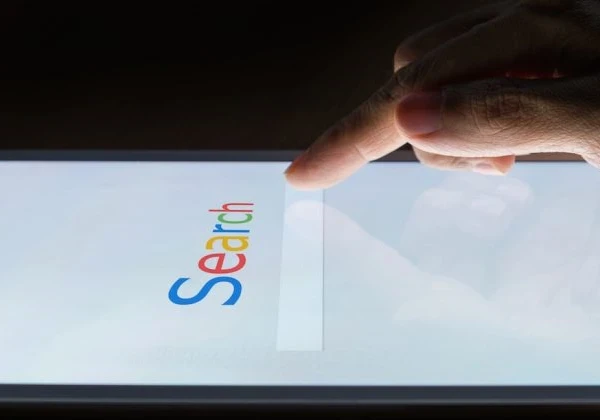 'Search' written in Google font and colours on a touchscreen with a user tapping the search bar