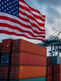 Header graphic for an EM360Tech news article showing a large US flag flying above shipping containers, port cranes and a cargo ship at a commercial seaport during sunrise or sunset. Overlaid text reads: "EM360TECH" and "US Rebuilds Global Tariff Wall With New Duties on 60 Trading Partners".
