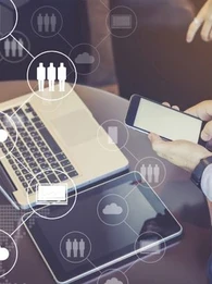 someone using a smartphone, with a macbook laptop and tablet next to them on a desk