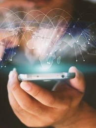 A person holding a smartphone while a graphic of the world's countries floats above the screen with various connecting lines from country to country