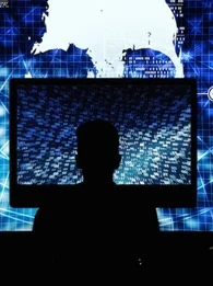 Hacker working on a large computer with additional screens next to them and a very large screen in front