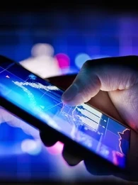 Hand holding a lit up smartphone with graphs on the screen in purple and blue.