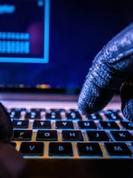 Gloved hands typing on a laptop to show a hacker working